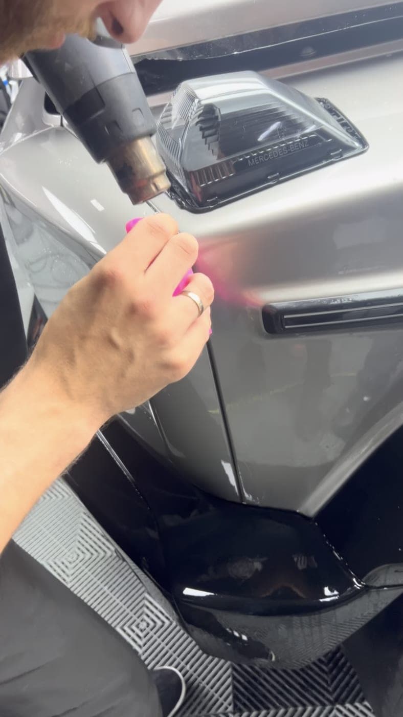 Heat gun and squeegee shaping film over a Mercedes fender