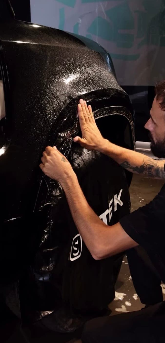 Installer smoothing film across a black rear quarter panel